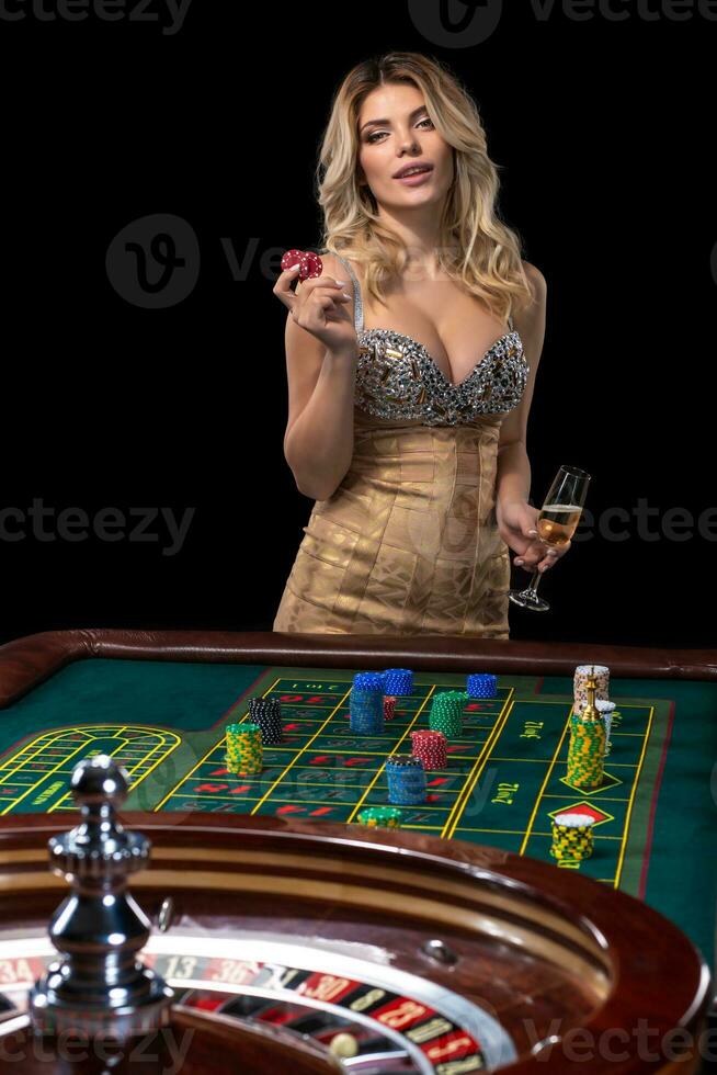 Young blonde woman wearing beautiful sexy shiny dress is playing roulette in the casino photo