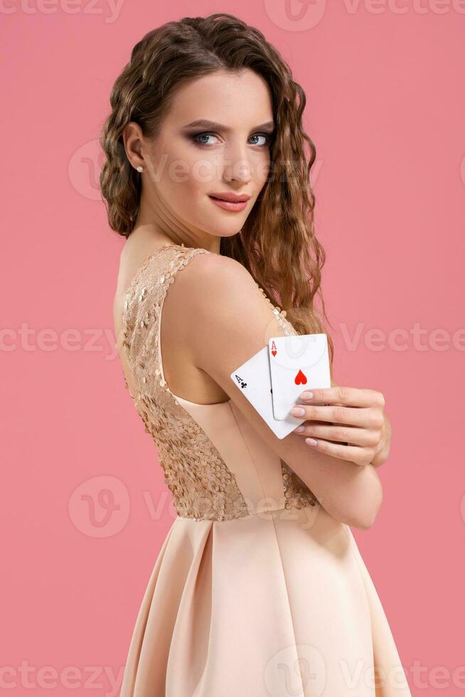 Young beautiful woman holding the winning combination of poker cards on pink background. Two aces photo