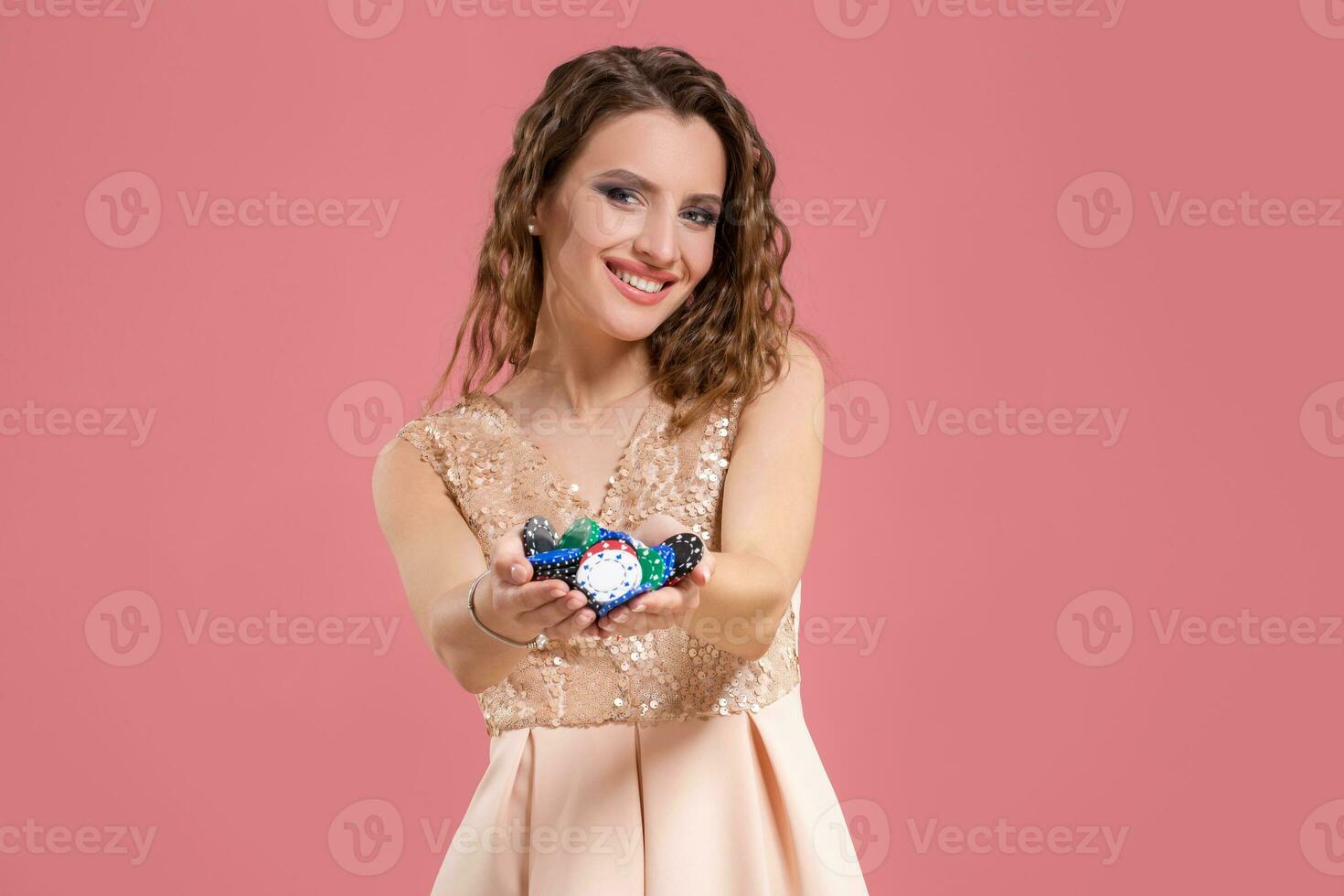 Young beautiful emotional woman with chips in hands on a pink background in the studio. Poker photo