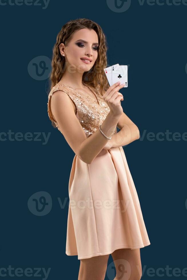 Young beautiful woman holding the winning combination of poker cards on dark blue background. Two aces photo