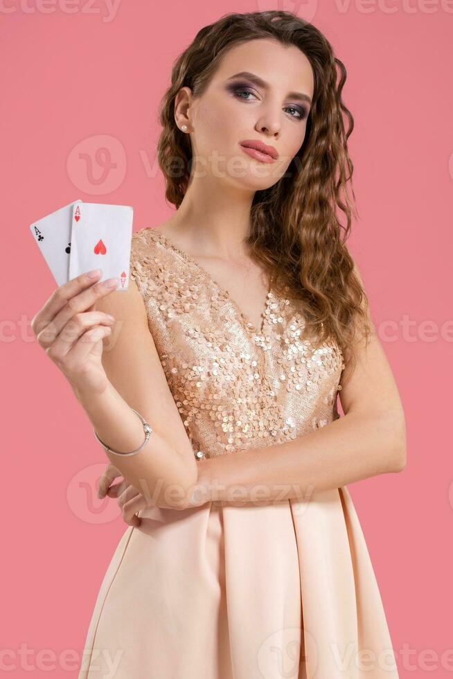 Young beautiful woman holding the winning combination of poker cards on pink background. Two aces photo