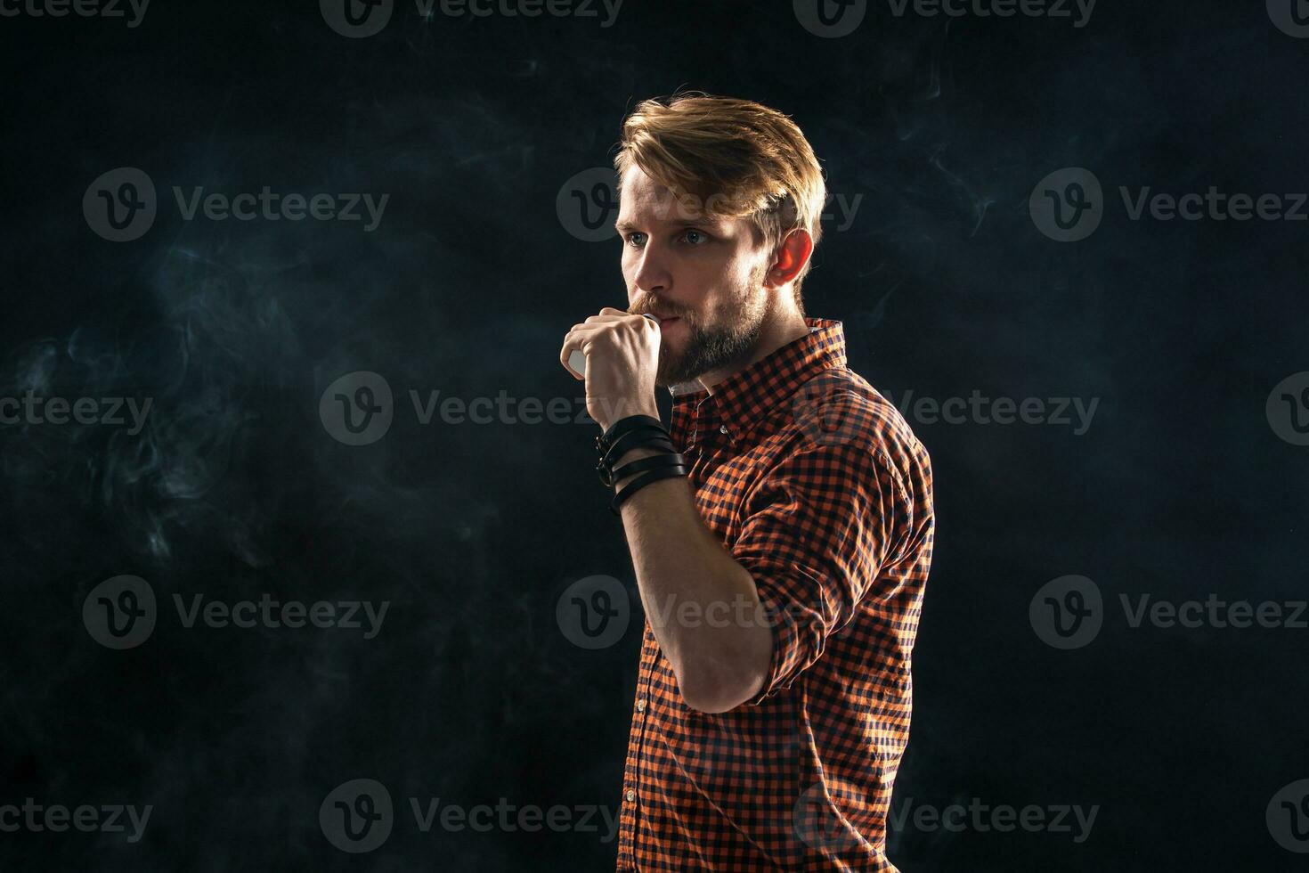 A young man with a beard and a stylish hairstyle in a shirt, smoking a cigarette, a viper, a room, a studio, smoke, enjoyment photo