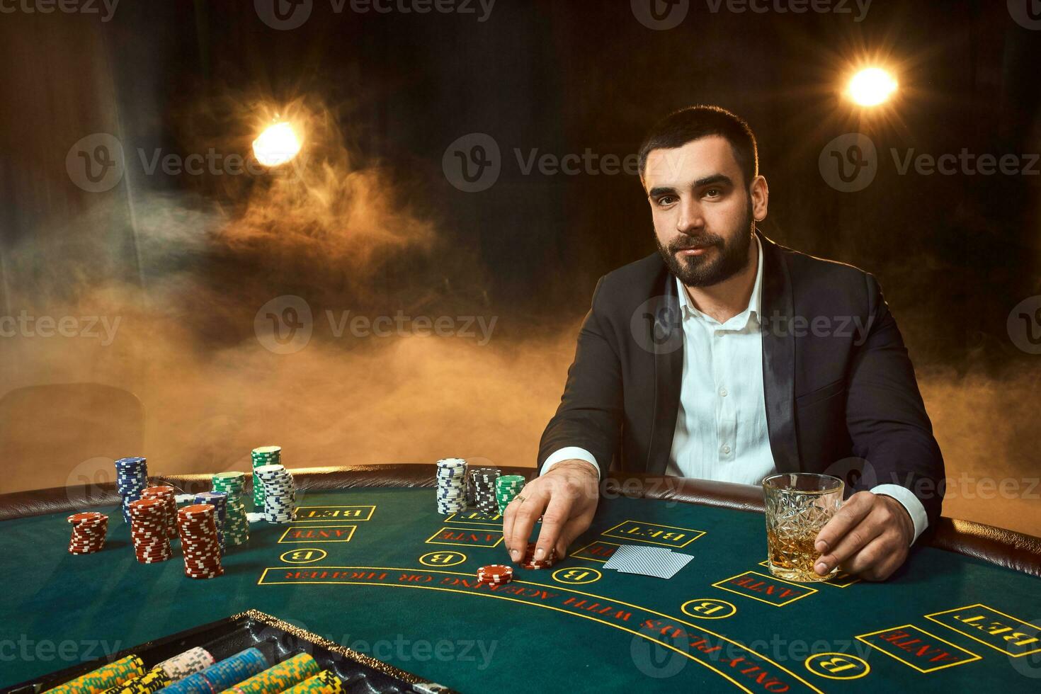 A young man in a business suit sitting at the poker table. Man gambles. The player at the gaming table playing cards. photo