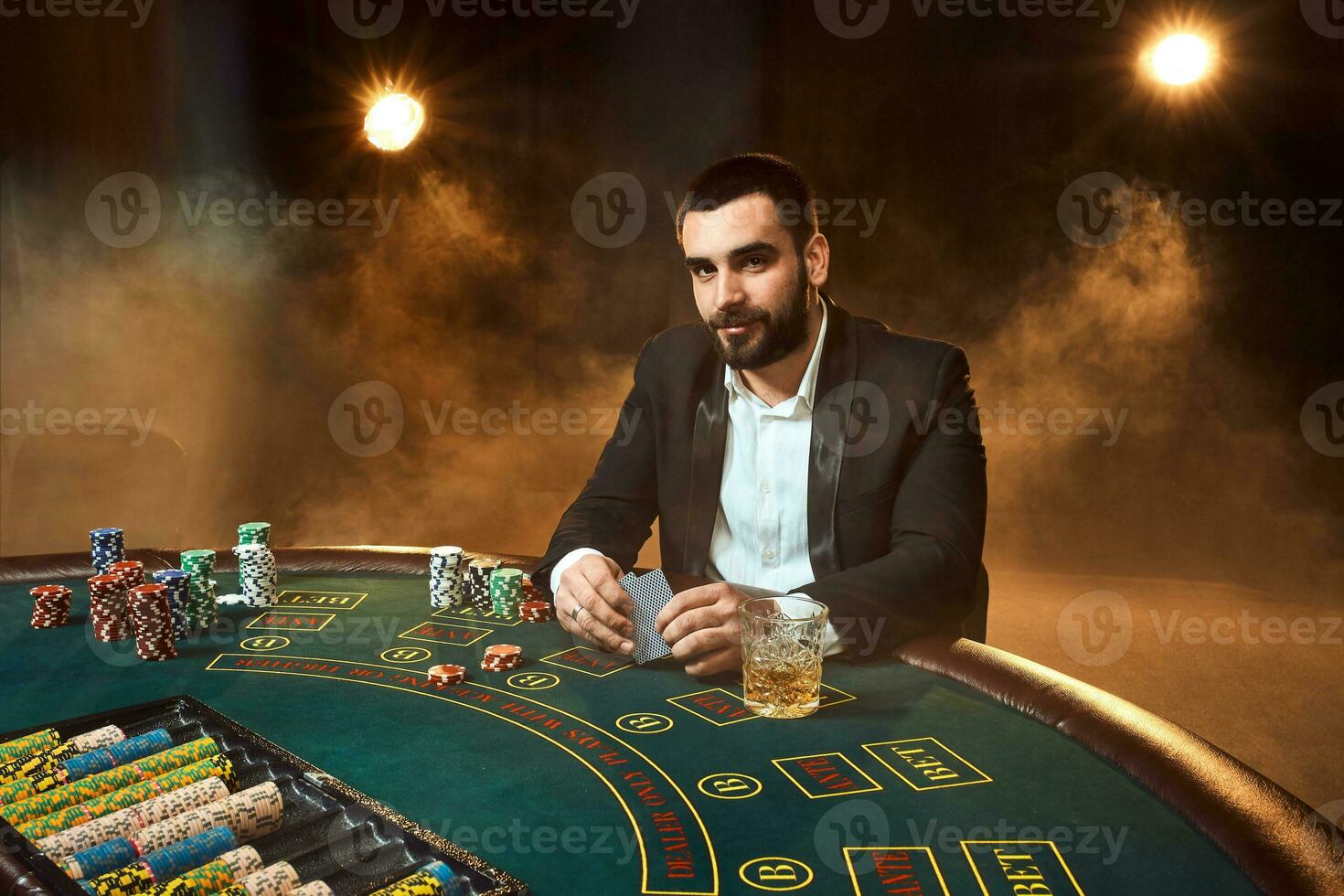 A young man in a business suit sitting at the poker table. Man gambles. The player at the gaming table playing cards. photo