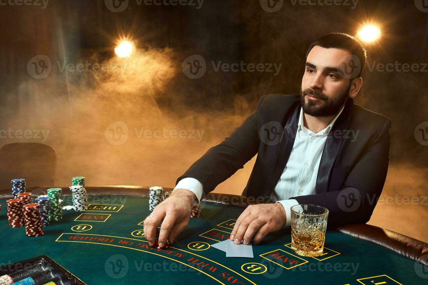 A young man in a business suit sitting at the poker table. Man gambles. The player at the gaming table playing cards. photo