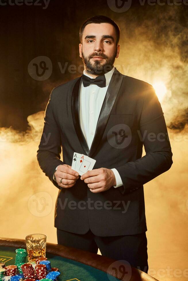 A young man in a business suit standing near poker table. Man gambles. photo