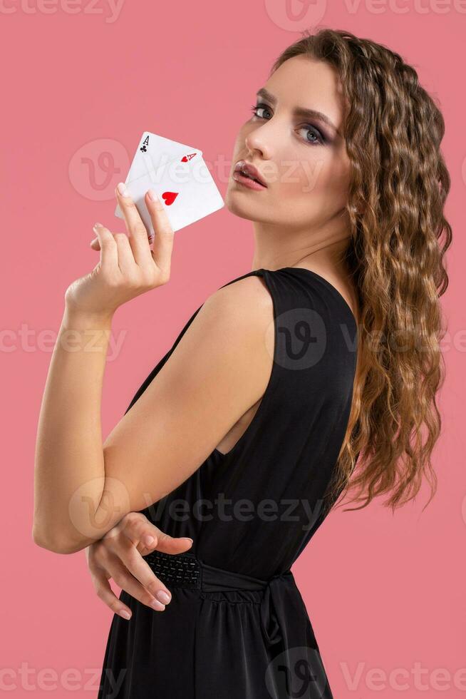 Young woman holding two aces in hand against on pink background photo