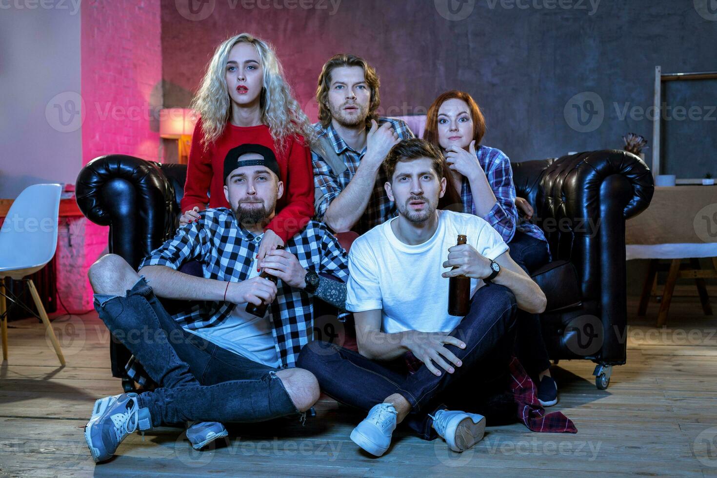 Five cheerful friends hanging out in an apartment and watching a photo