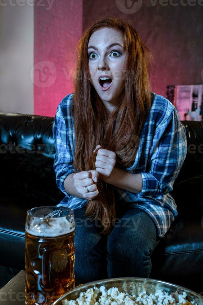 Emotional beautiful woman watching football, sitting in living r photo