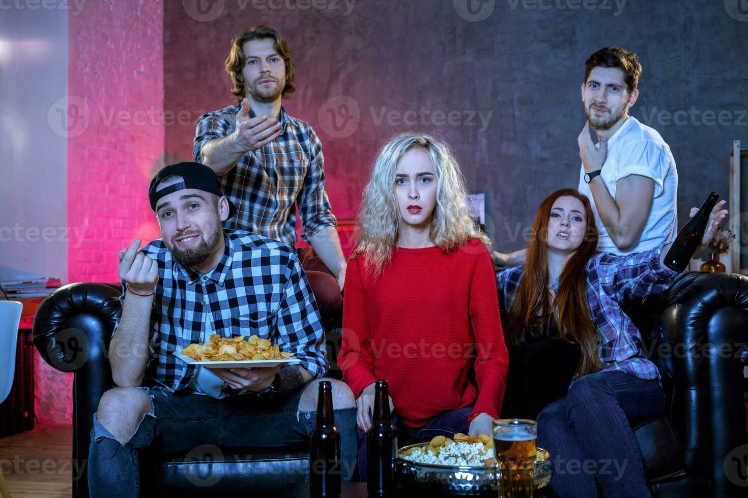 Five cheerful friends hanging out in an apartment and watching a photo