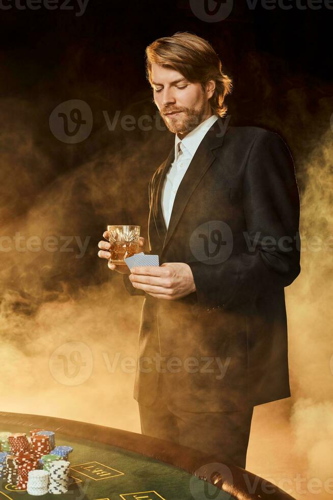 A man in a business suit standing near the game table. Male player. Passion, cards, chips, alcohol, dice, gambling, casino - it is as male entertainment. photo