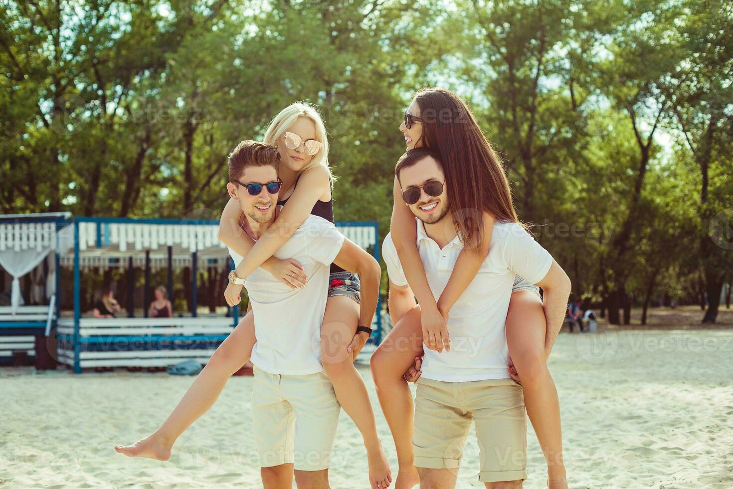Group of friends walking along the beach, with men giving piggyback ride to girlfriends. photo