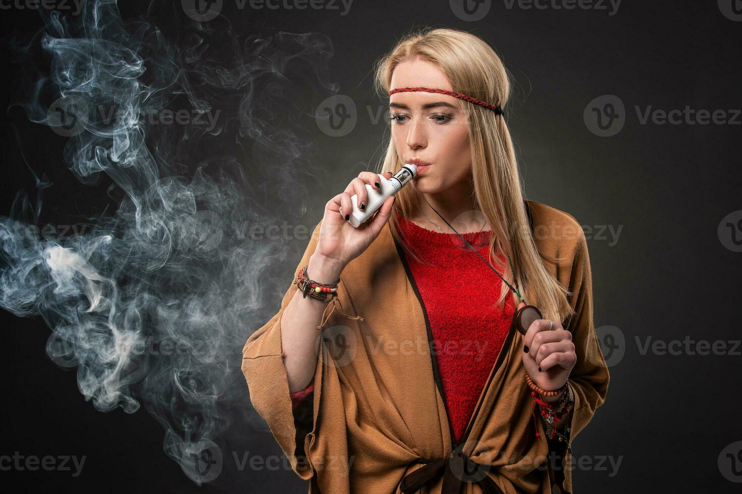 Portrait of sexy young hipster smoking vaping girl. The woman is dressed in the style of a boho. Vapor concept. Vaping e-Cigarette. photo