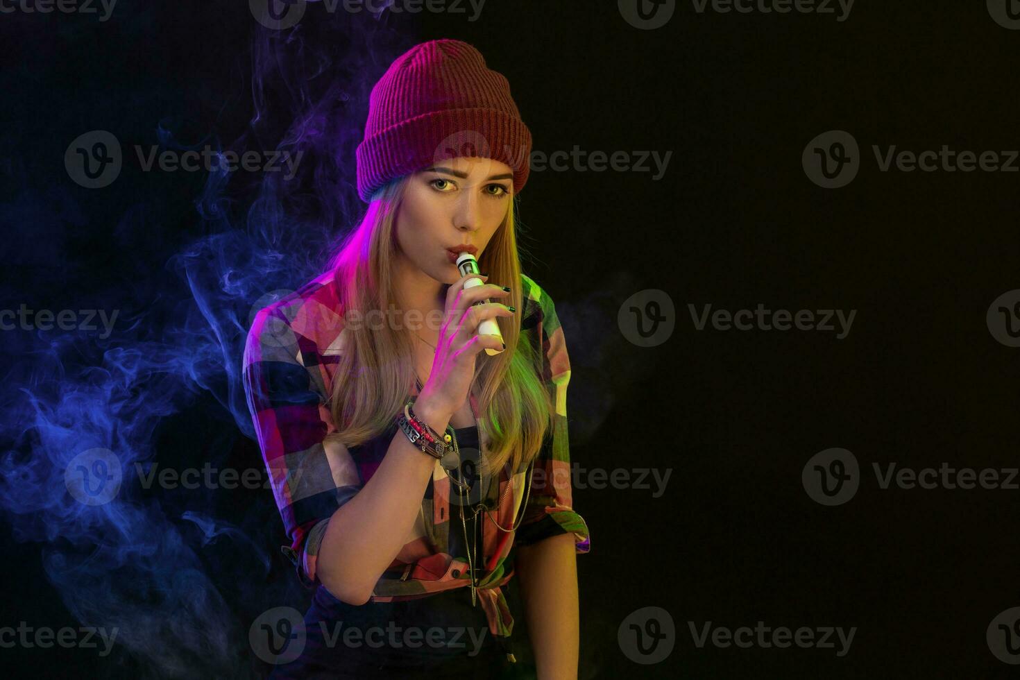 Vaping girl. Young hipster woman vape e-cig on black background. Hip-hop style. Studio shot photo