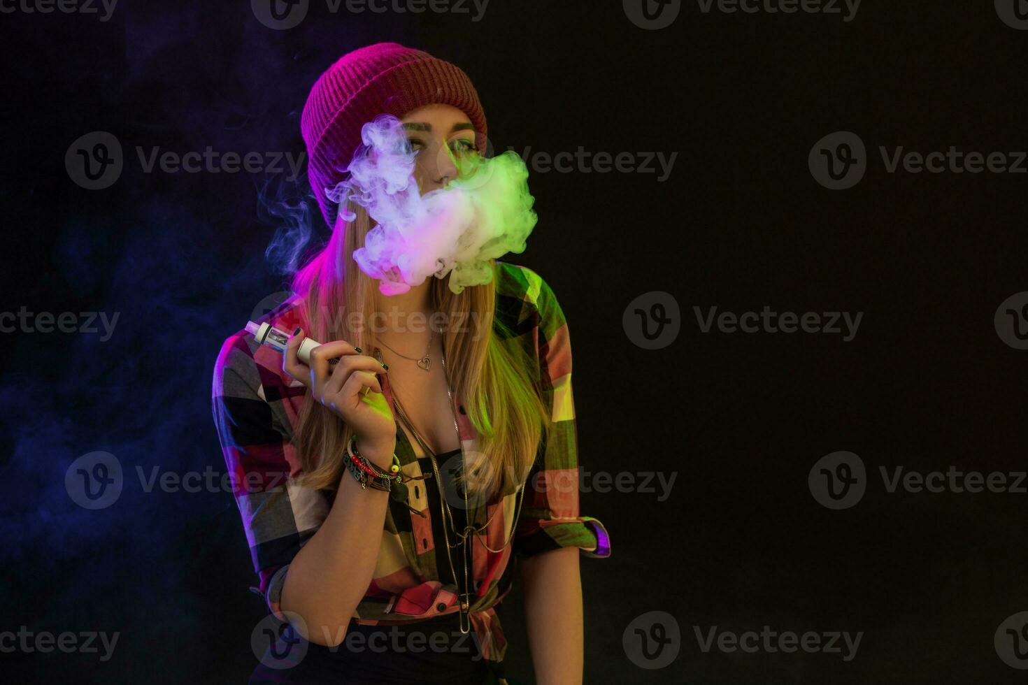 Vaping girl. Young hipster woman vape e-cig on black background. Hip-hop style. Studio shot photo