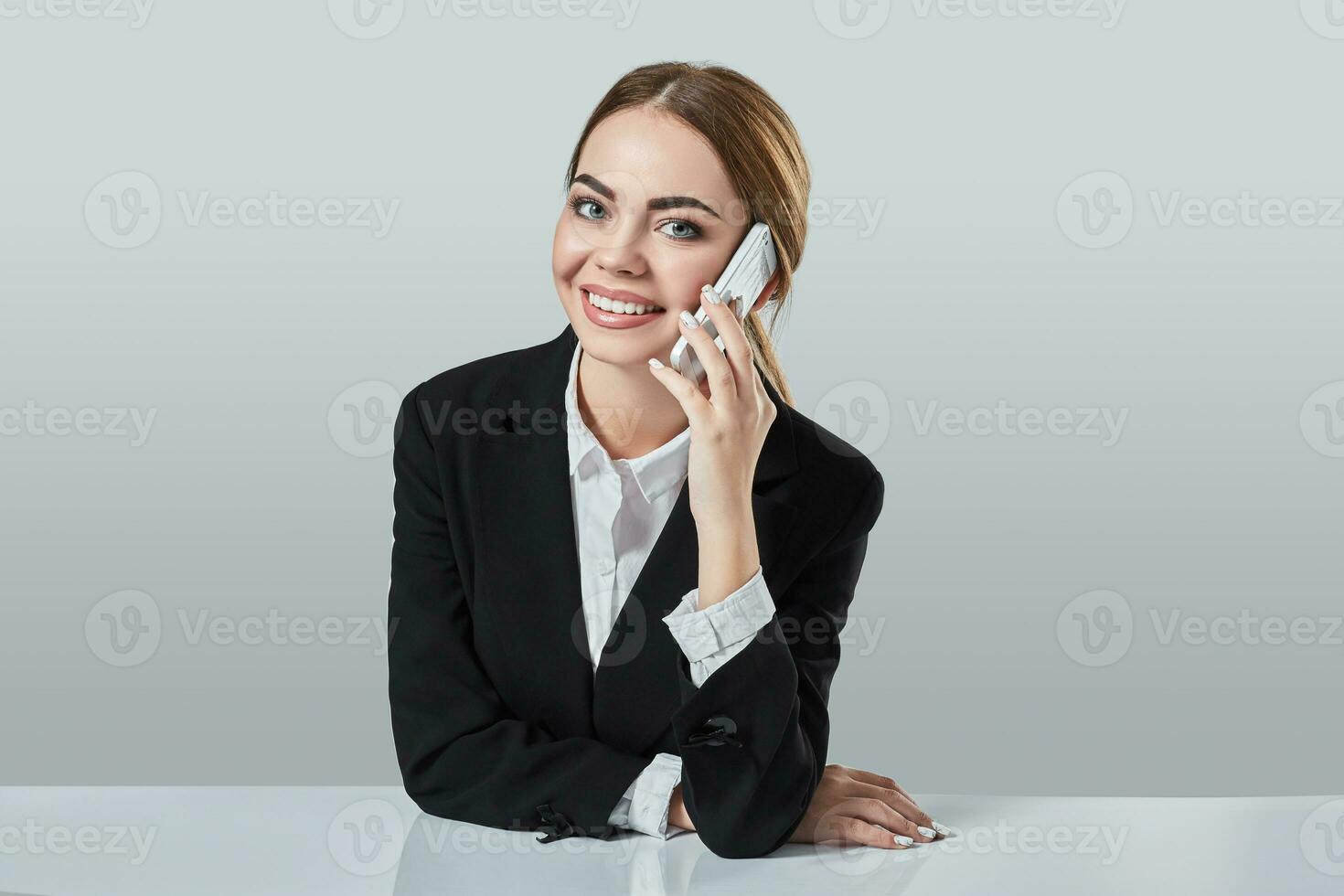 attractive dark-haired woman dressed in a black suit is sitting at  table in an office. photo