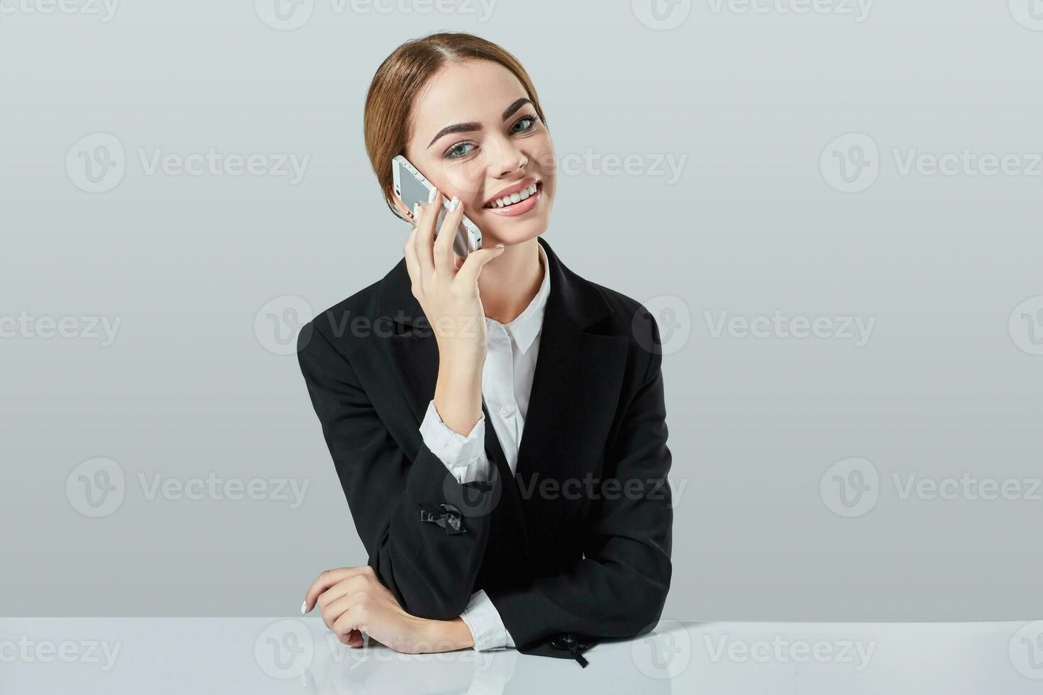 attractive dark-haired woman dressed in a black suit is sitting at  table in an office. photo