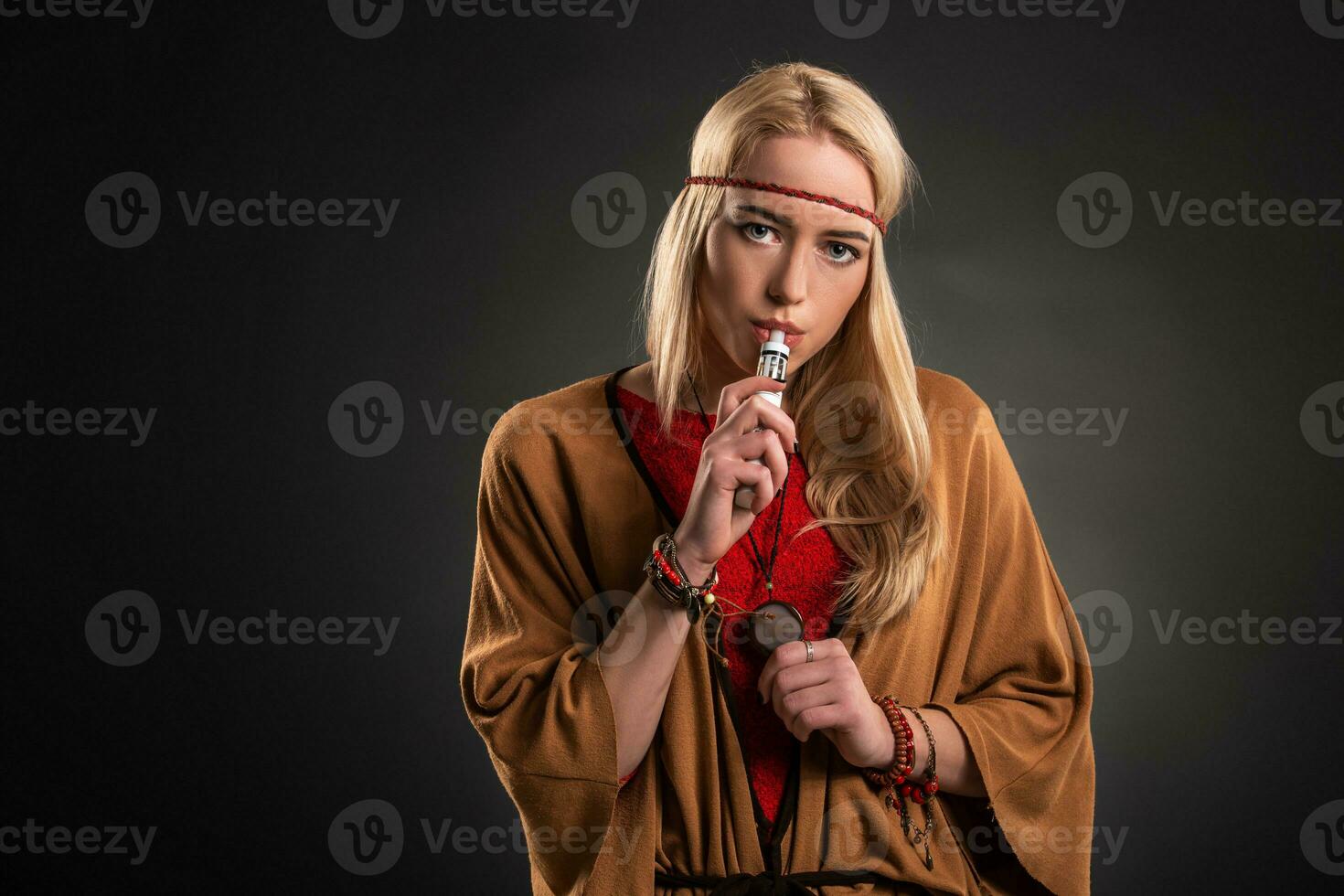 Portrait of sexy young hipster smoking vaping girl. The woman is dressed in the style of a boho. Vapor concept. Vaping e-Cigarette. photo