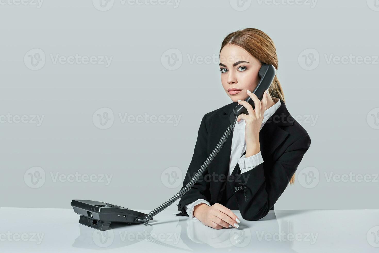 attractive dark-haired woman dressed in a black suit is sitting at  table in an office. photo