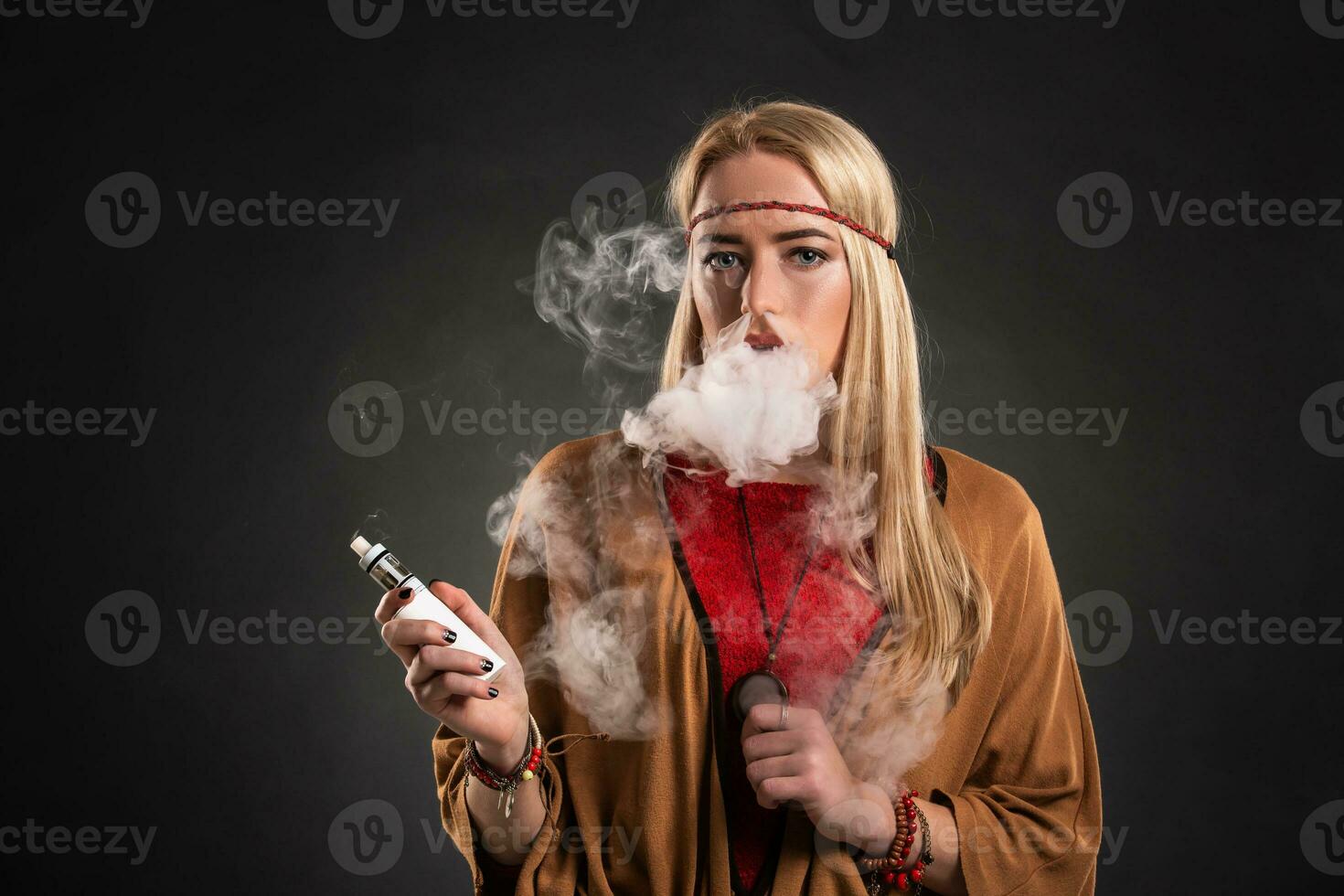 Portrait of sexy young hipster smoking vaping girl. The woman is dressed in the style of a boho. Vapor concept. Vaping e-Cigarette. photo