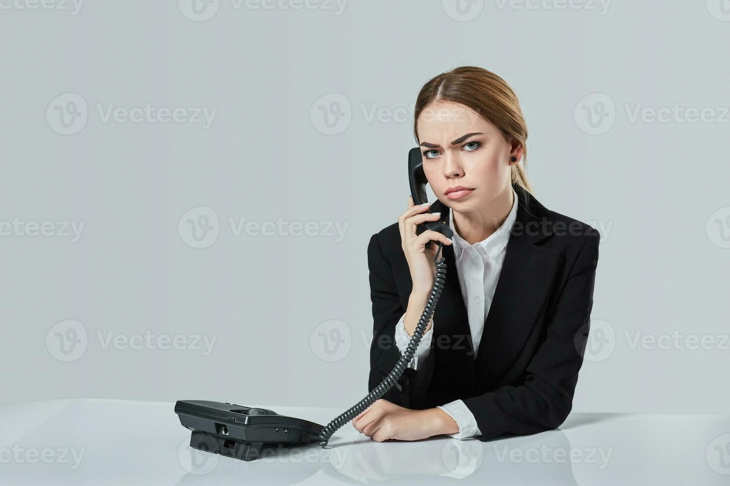 attractive dark-haired woman dressed in a black suit is sitting at  table in an office. photo