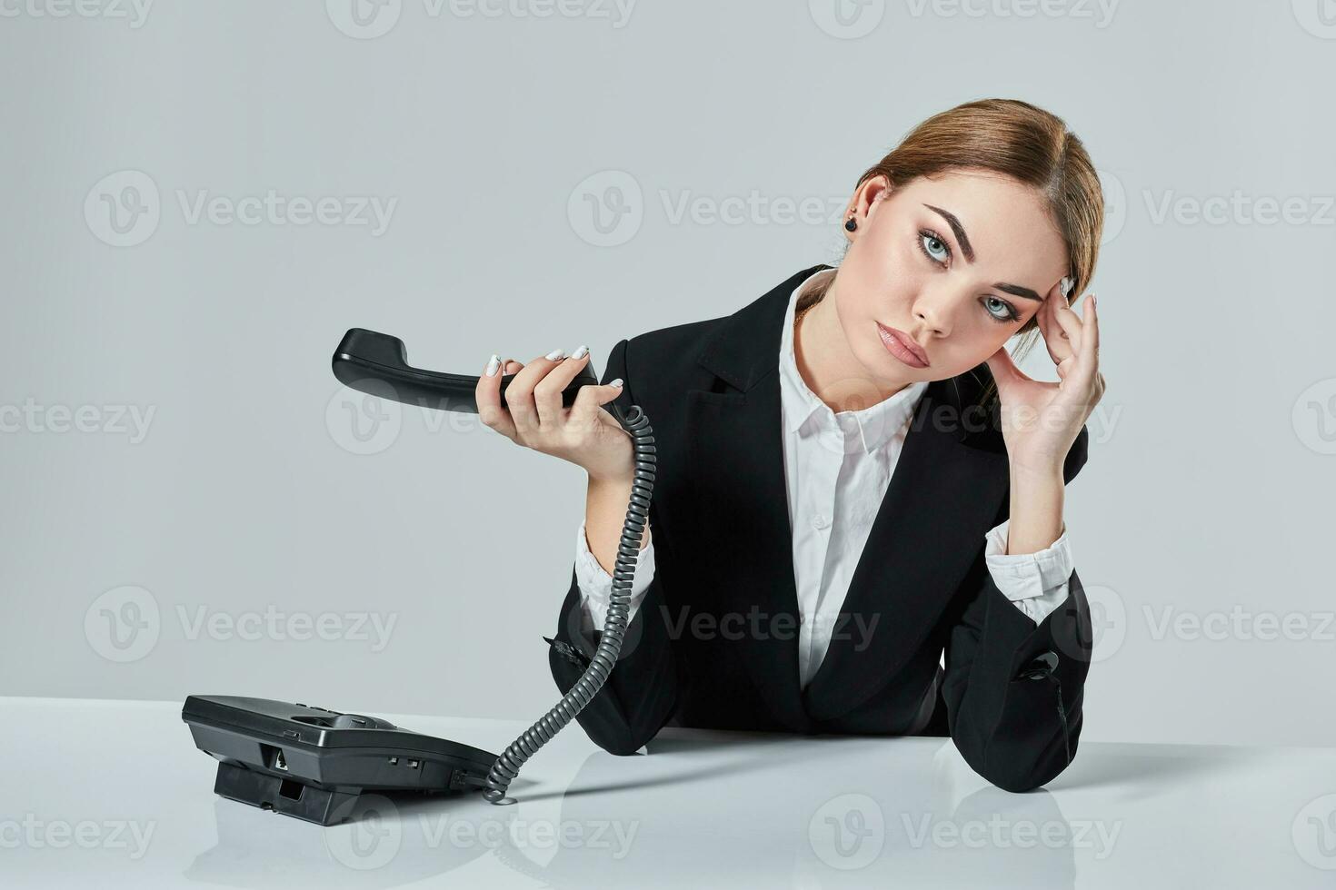 attractive dark-haired woman dressed in a black suit is sitting at  table in an office. photo