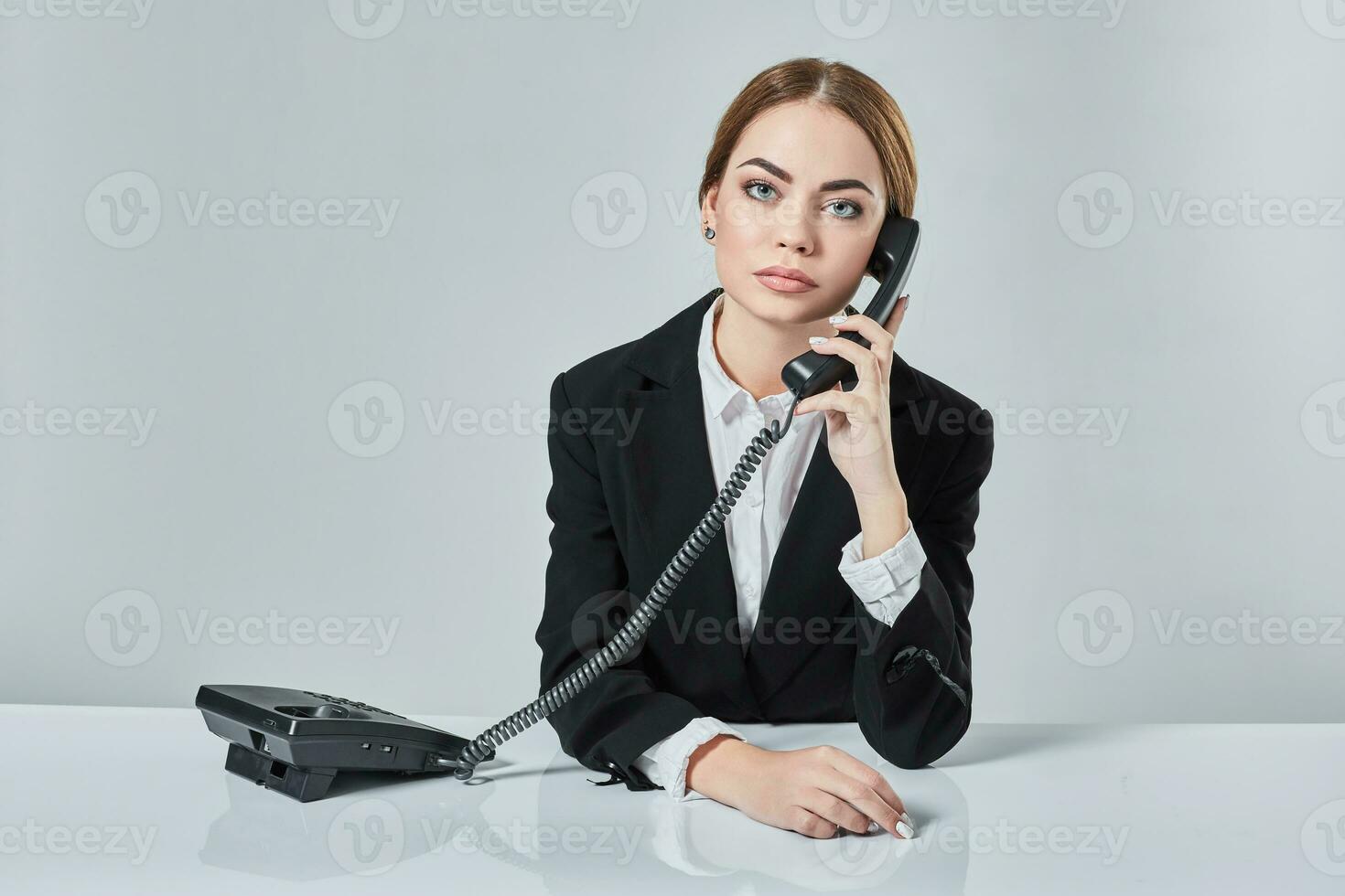 attractive dark-haired woman dressed in a black suit is sitting at  table in an office. photo