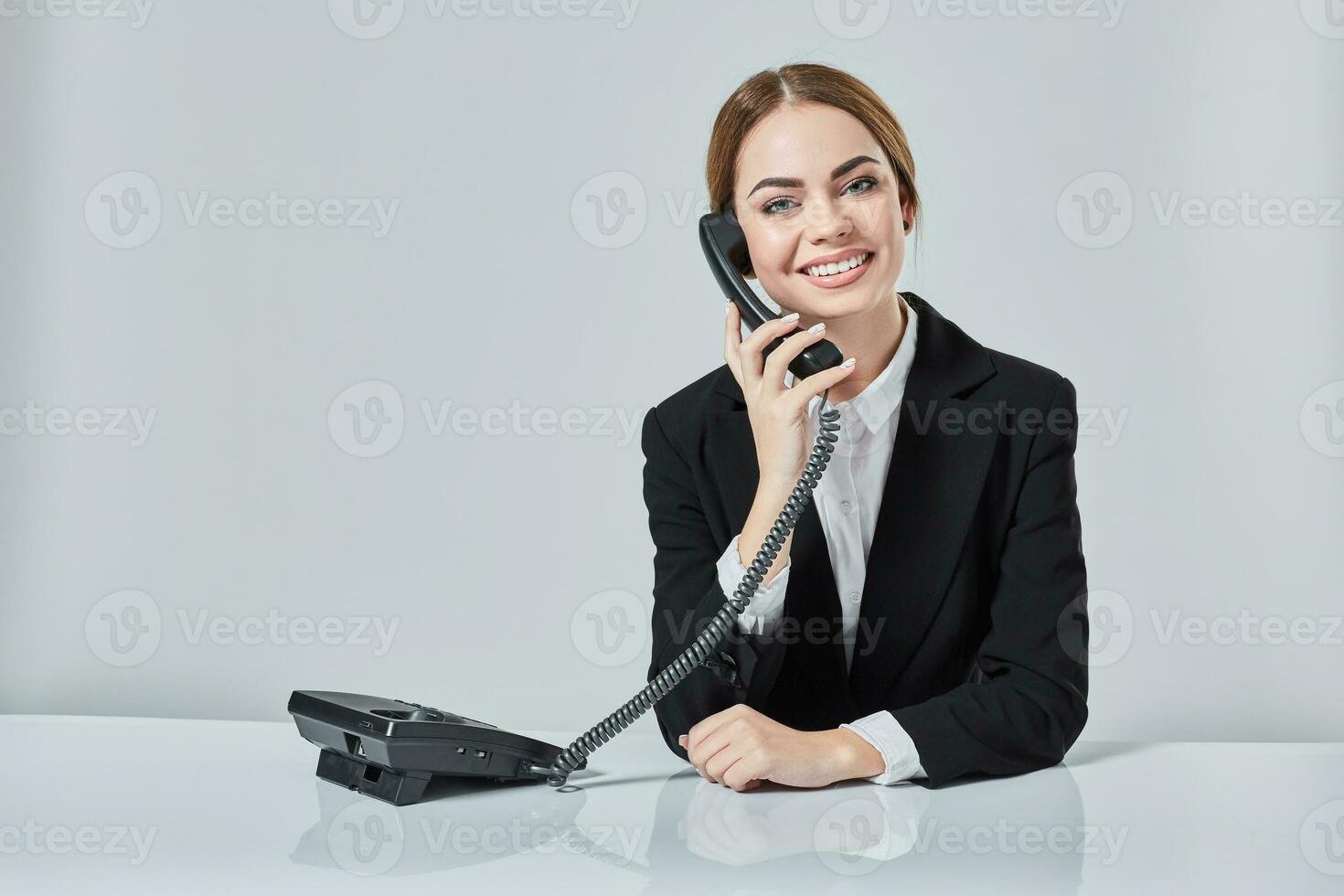 attractive dark-haired woman dressed in a black suit is sitting at  table in an office. photo