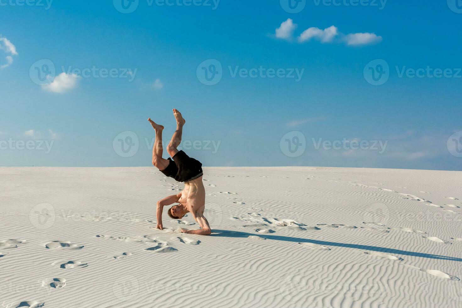 Young sporty man want doing acrobatic exercises on the sand near river photo