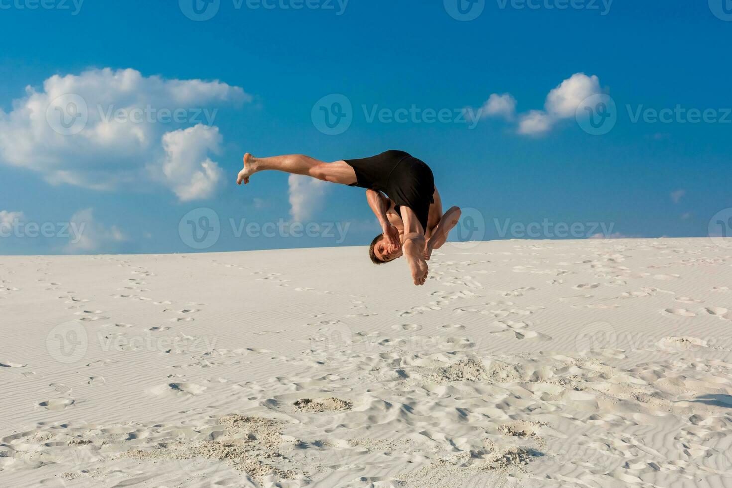 Portrait of young parkour man doing flip or somersault on the sand. photo