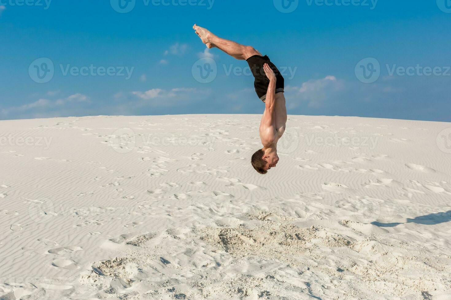 Portrait of young parkour man doing flip or somersault on the sand. photo