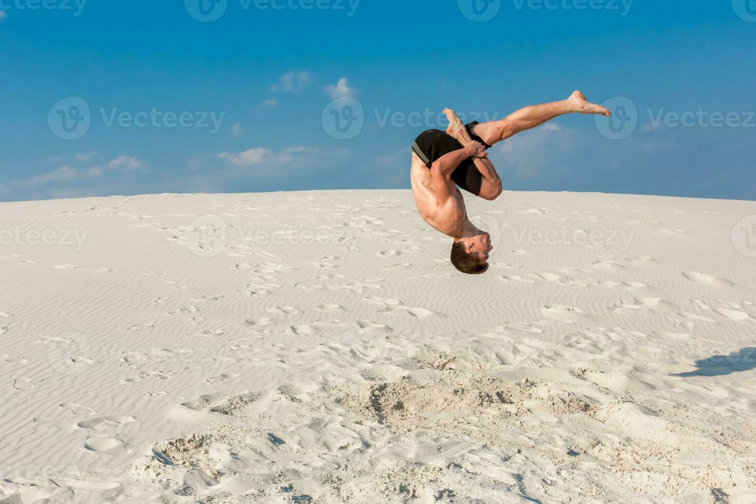 Portrait of young parkour man doing flip or somersault on the sand. photo