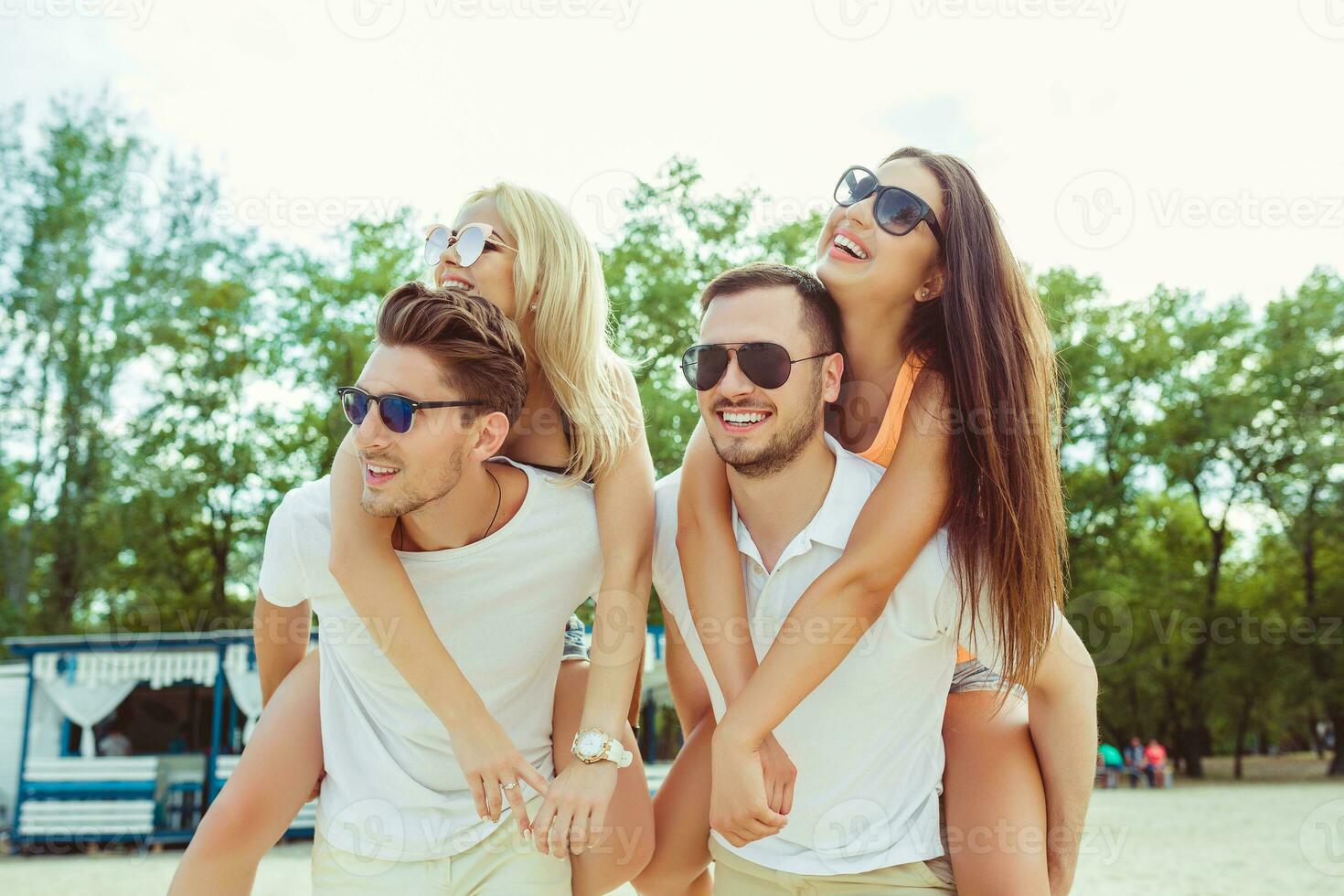 Group of friends walking along the beach, with men giving piggyback ride to girlfriends. photo