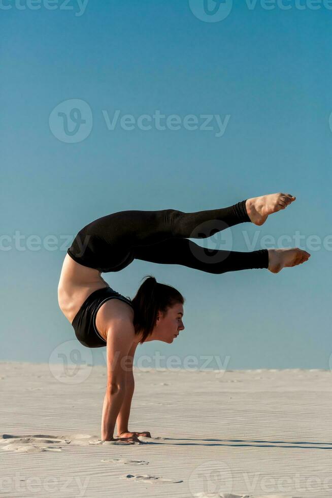 Young woman practicing handstand on beach with white sand and bright blue sky photo