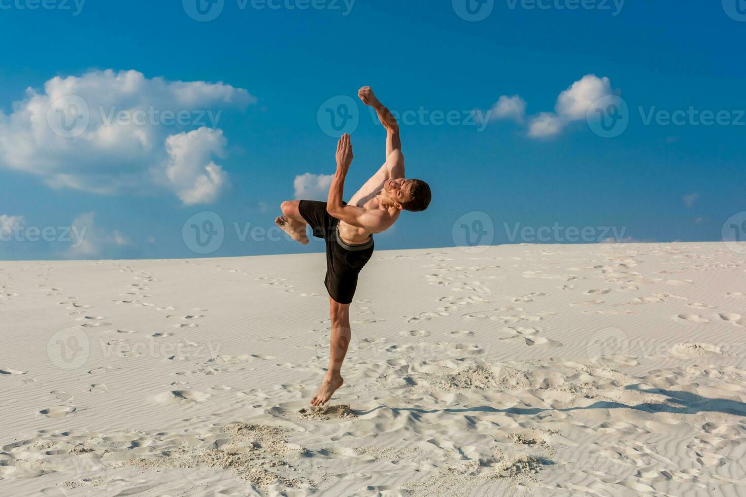 Portrait of young parkour man doing flip or somersault on the sand. photo