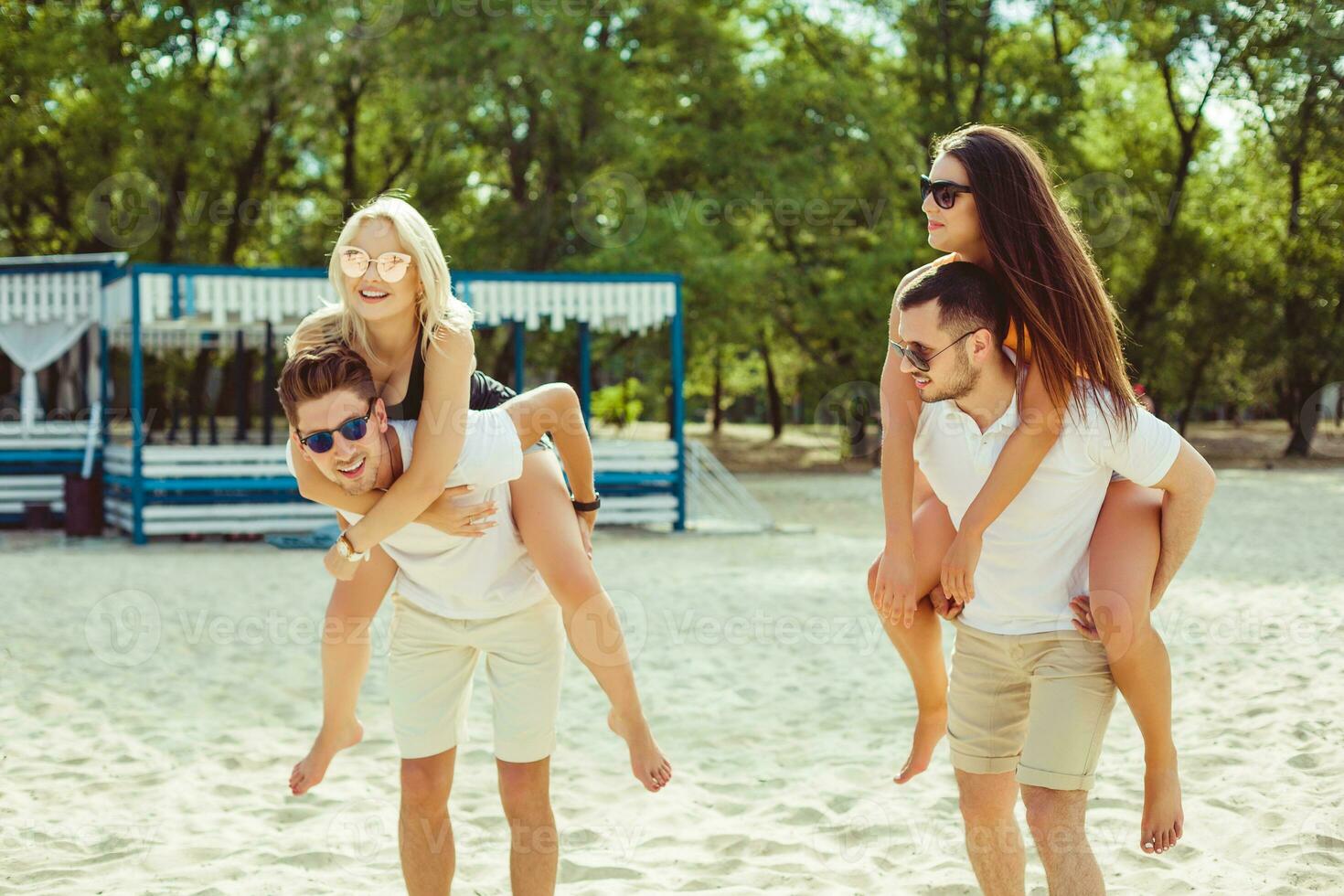 Group of friends walking along the beach, with men giving piggyback ride to girlfriends. photo
