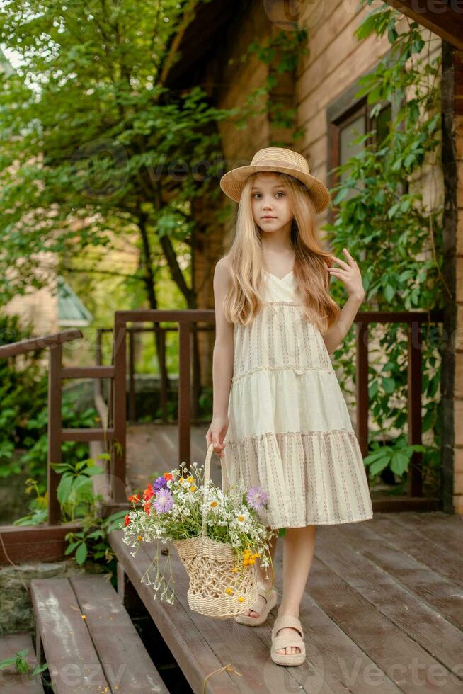 Carefree tween girl with basket of wildflowers standing on doorstep of country house photo