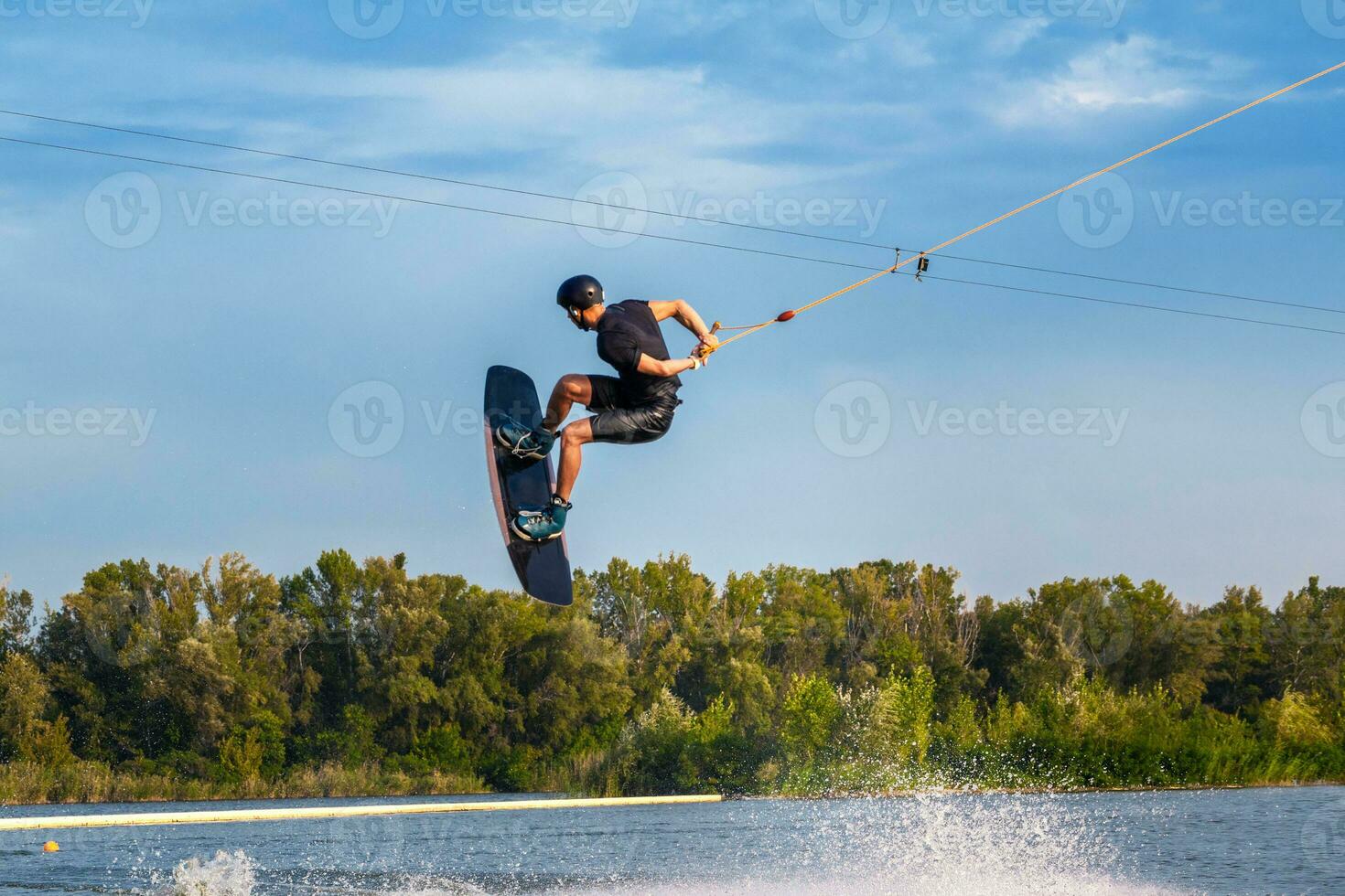 Skilled male wakeboarder jumping with backside rotation over water holding rope in hand photo