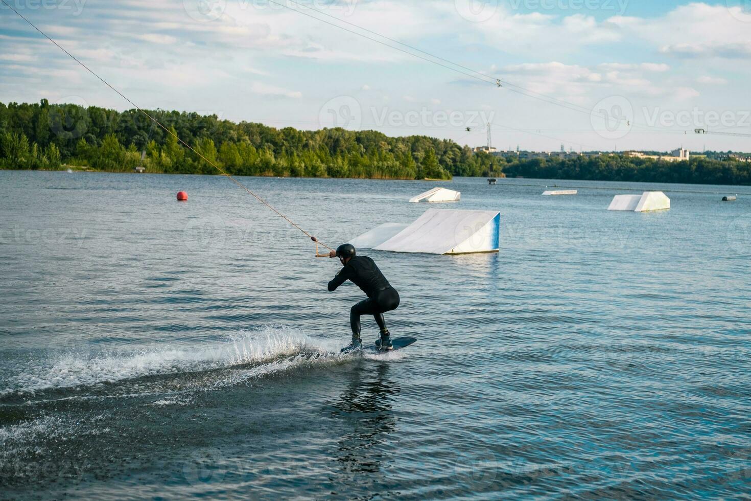 Wakeboarder sliding on water on board getting ready to perform ramp jump photo
