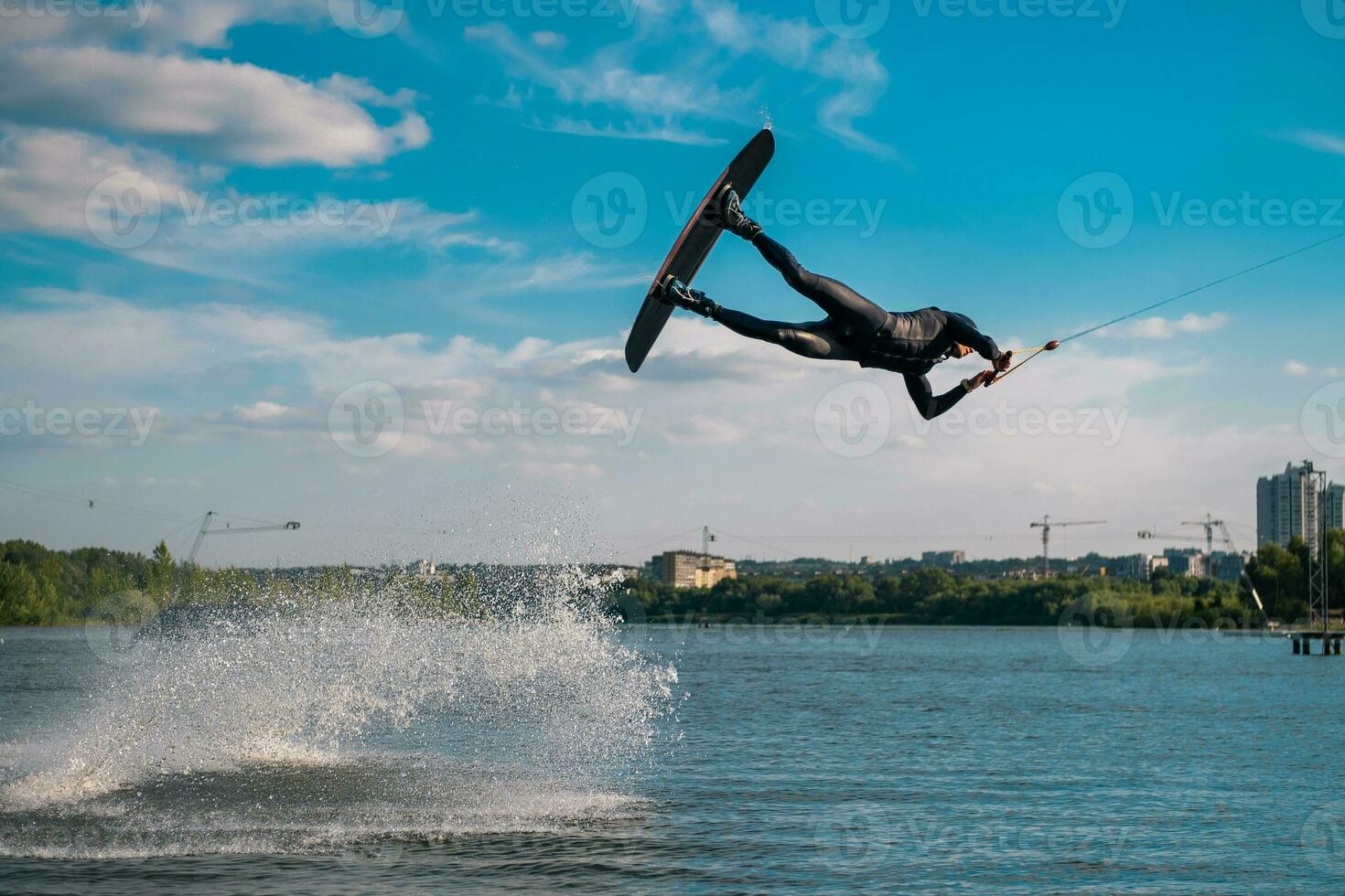 Professional wakeboarder performing jump over water while holding on tow rope photo