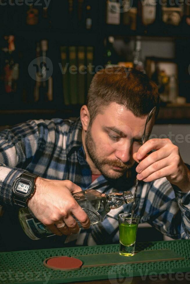 Bartender pouring tequila down spiral stem of bar spoon into shot glass with banana liqueur photo