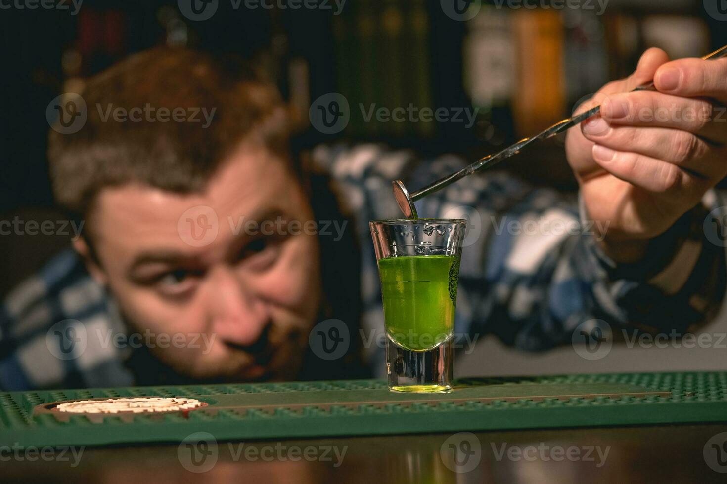 Bartender taking out bar spoon from shot glass with green drink photo