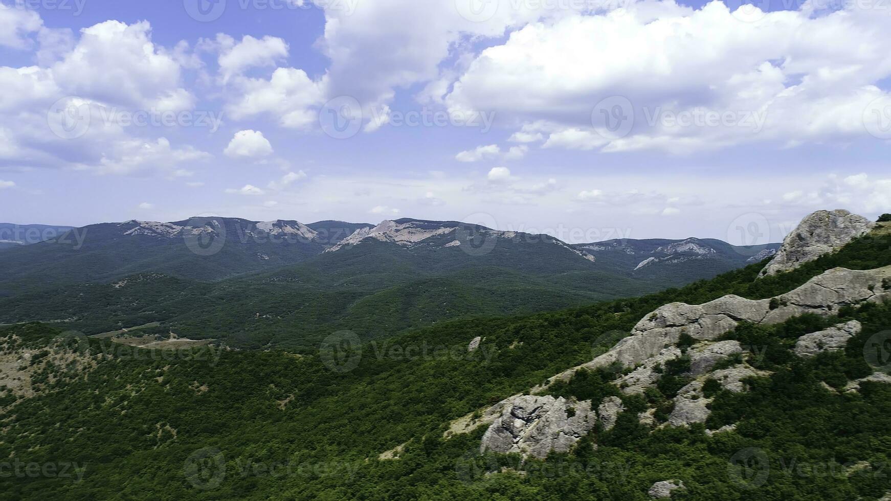 Aerial view of mountain rocks with a vast valley on blue cloudy sky background. Shot. Natural breathtaking landscape with green trees, rocks, and hills. photo