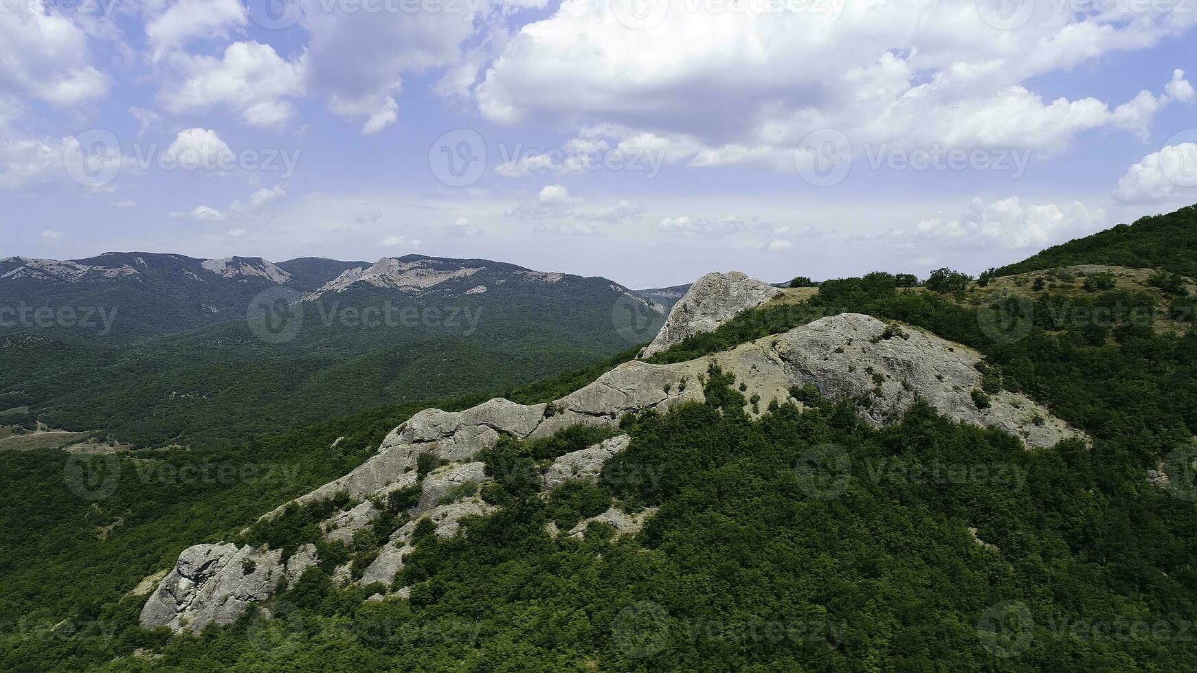 Aerial view of hilly region with mountains on the background of blue sky with clouds. Shot. Flying over the mountains covered dense green forest and rock formations. photo