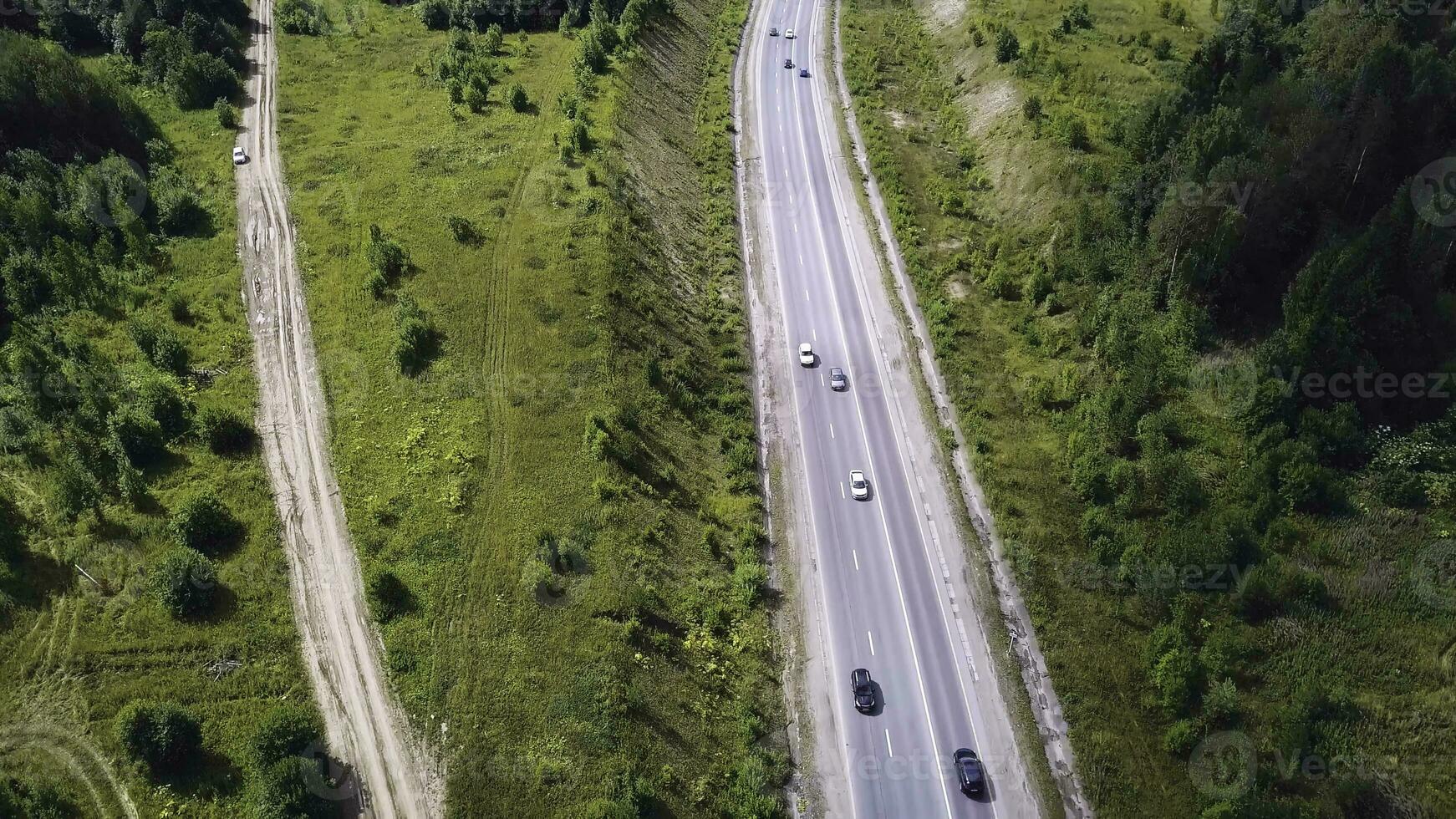 Aerial top view of summer green trees, river, roads in forest background. Aerial view of crooked path of road on the mountain. Clip. Aerial view of cars driving on country road in forest. The aerial photo