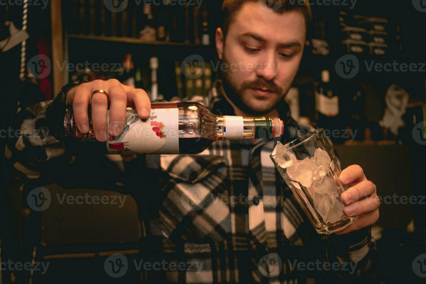 Bartender pouring grenadine syrup from bottle into glass with ice, preparing Tequila Sunrise cocktail photo