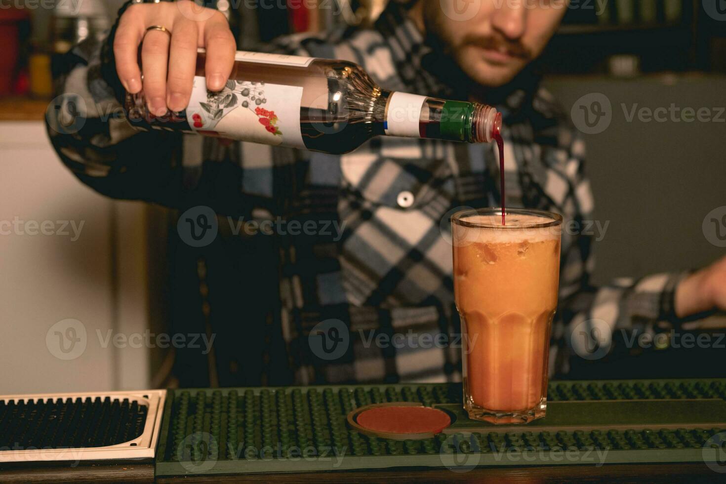 Bartender preparing Tequila Sunrise cocktail, adding pomegranate syrup into glass with drink photo