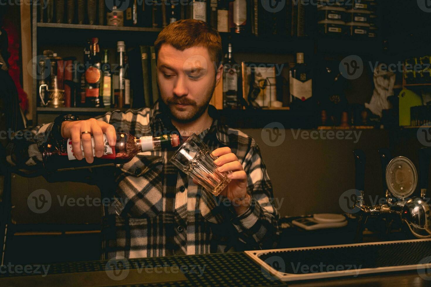Bartender pouring pomegranate syrup from bottle into highball glass photo