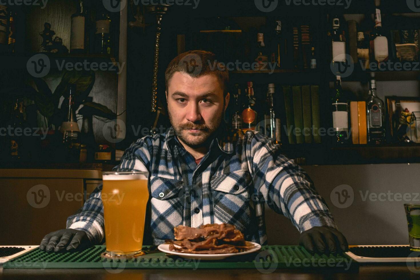 Bartender standing behind bar counter in pub with glass of beer and plate of snacks photo