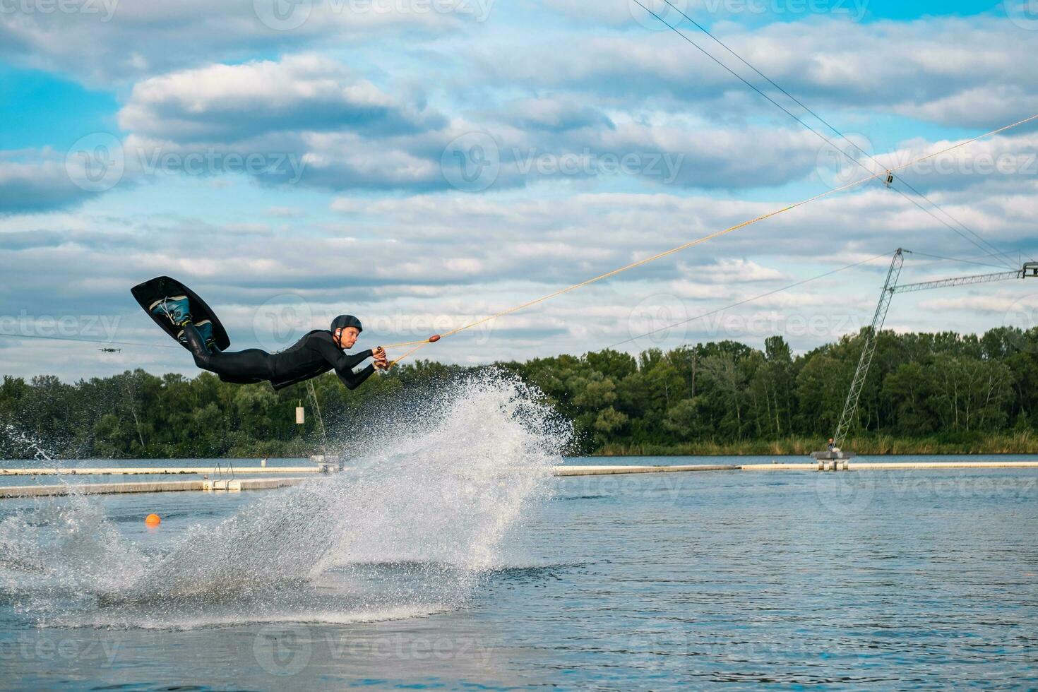 Experienced male wakeboarder performing jump over water holding on towing cable photo